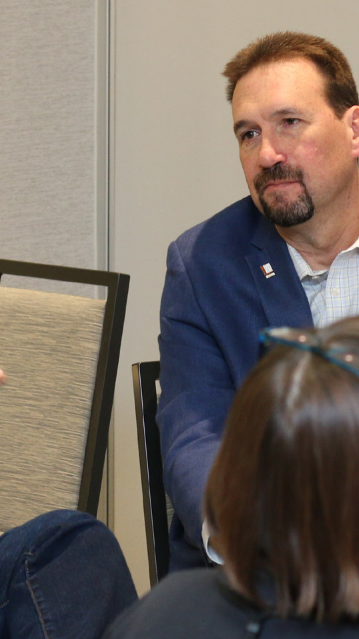 Tony Wasley speaking during a breakout group discussion at a conference table, with three other attendees listening.